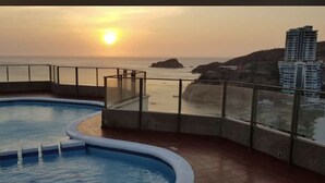 En pool på taket med utsikt över havet och byggnaderna vid solnedgången.