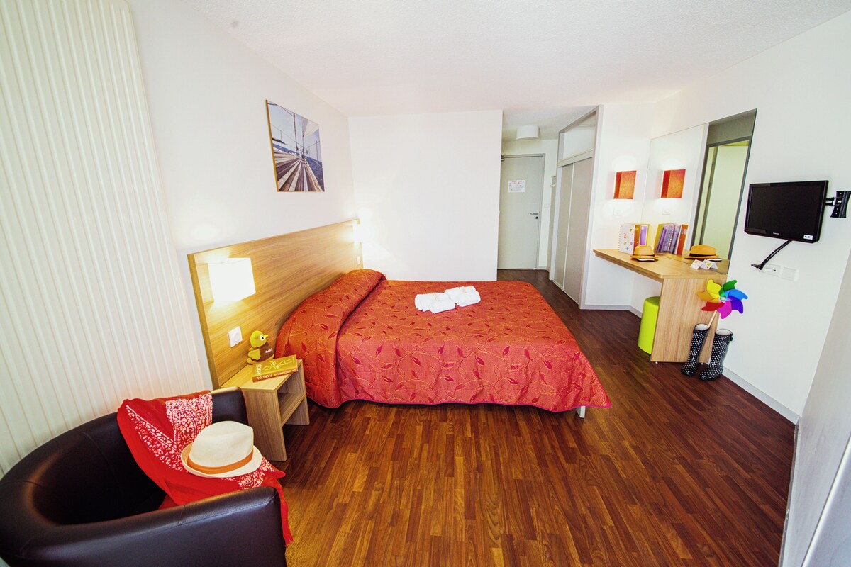 A hotel room with a bed, a desk with a chair, a television, and a mirror.