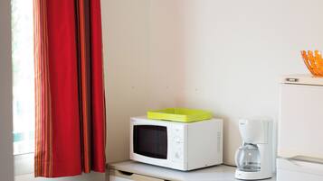 A dining area with a table, chairs, a microwave, a coffee maker, and a window with curtains.