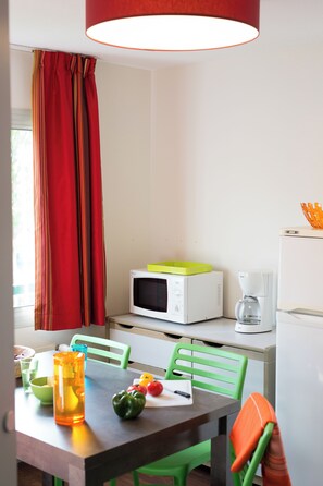 Un coin repas comprenant une table, des chaises, un four à micro-ondes, une machine à café et une fenêtre avec des rideaux.