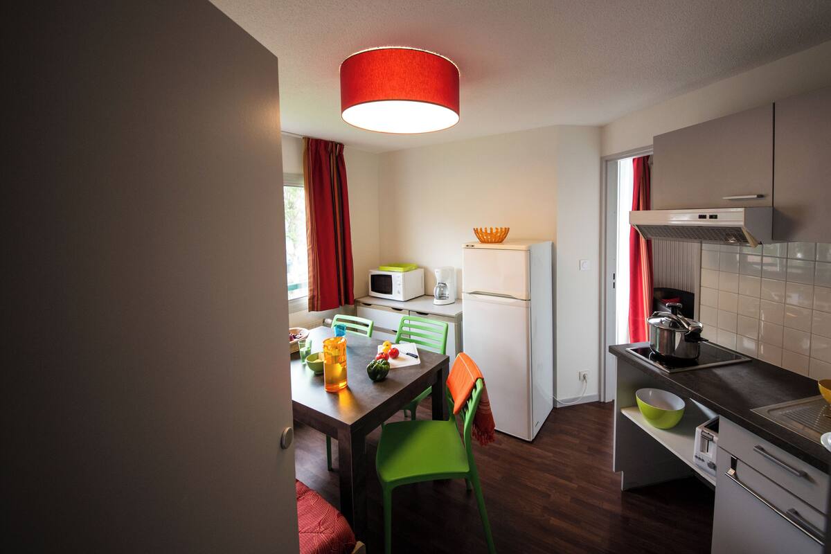 Cocina compacta con mesa, sillas, microondas, refrigerador y estufa.