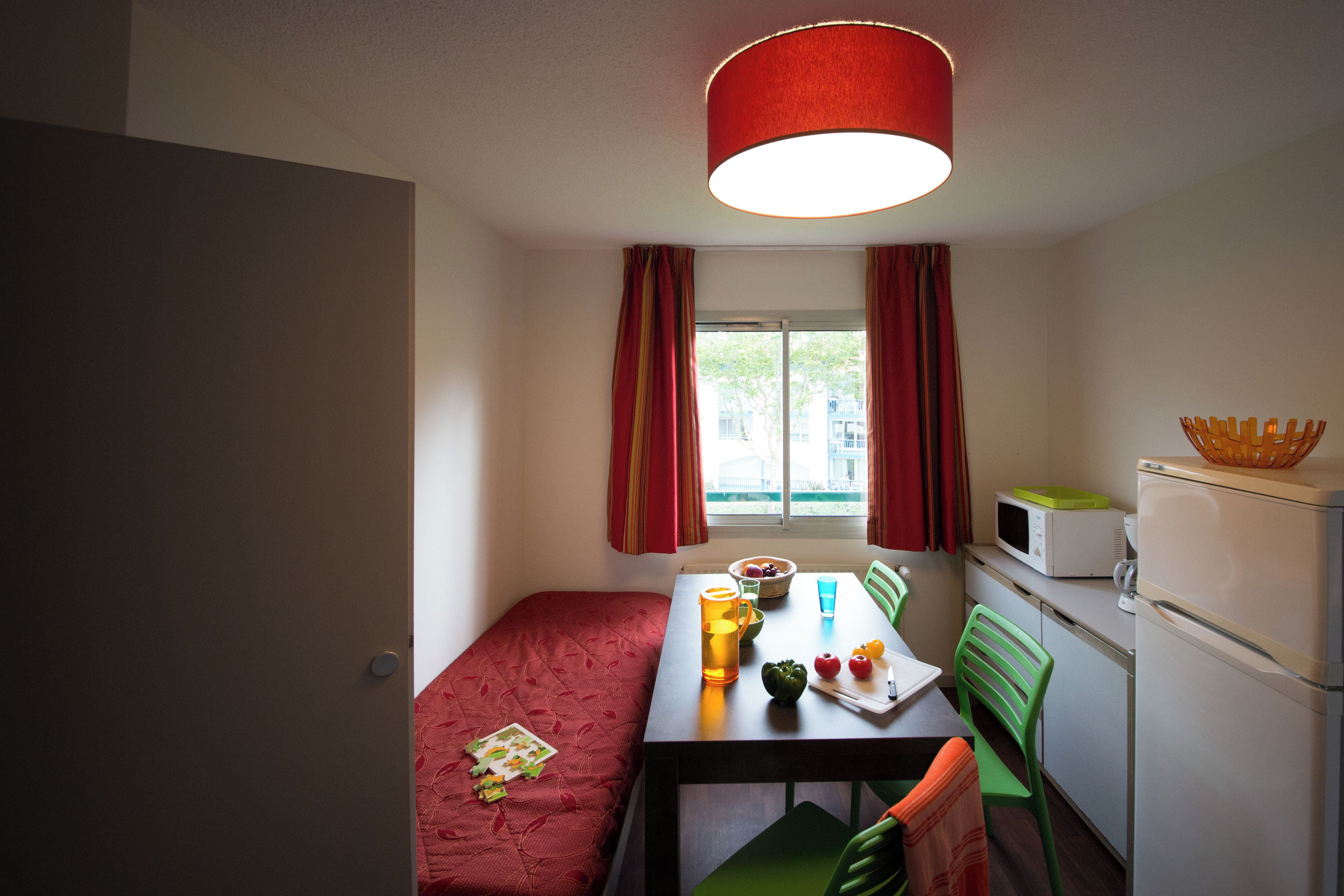 Una habitación compacta con cama, una mesa de comedor, sillas, microondas y refrigerador.
