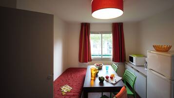 Una habitación compacta con cama, una mesa de comedor, sillas, microondas y refrigerador.