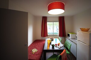 Una habitación compacta con cama, una mesa de comedor, sillas, microondas y refrigerador.