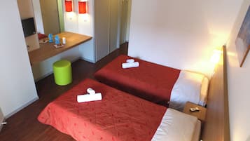 Una habitación de hotel con dos camas, un escritorio pequeño, un cubo de basura verde y una televisión.