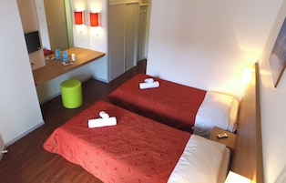 Una habitación de hotel con dos camas, un escritorio pequeño, un cubo de basura verde y una televisión.