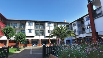 Un patio con un edificio que tiene varios balcones, una palmera y macizos de flores.
