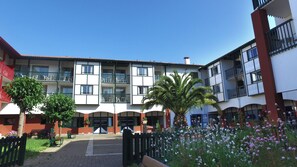 A courtyard with a building featuring multiple balconies, a palm tree, and flower beds.