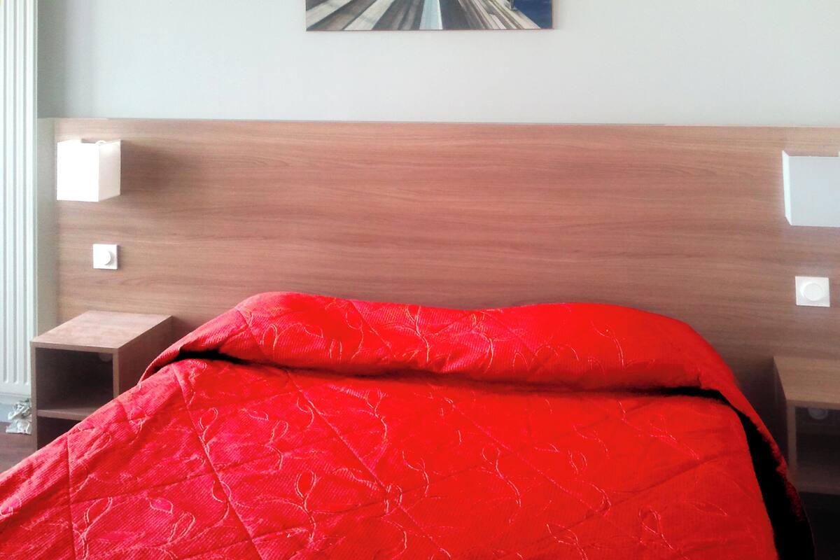 Una habitación de hotel con cabecera de madera, colcha roja y un cuadro en la pared.