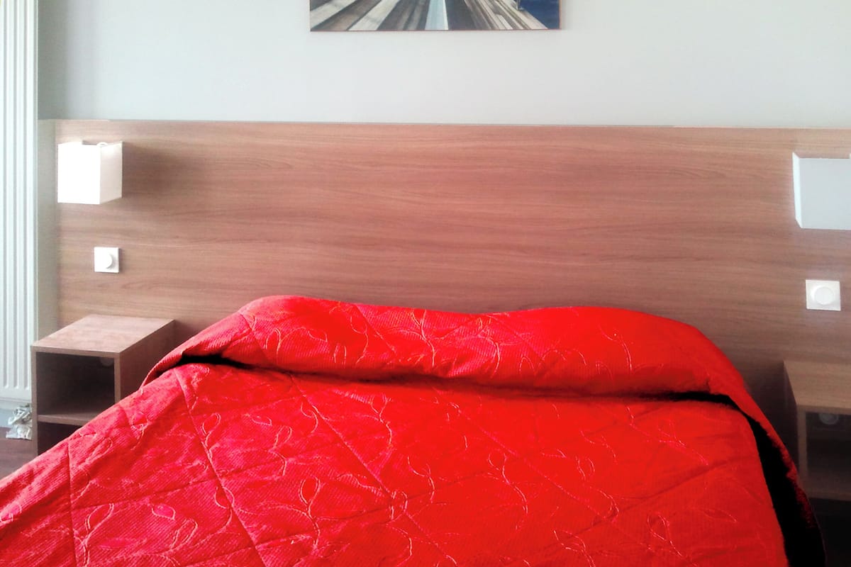 Una habitación de hotel con cabecera de madera, colcha roja y un cuadro en la pared.
