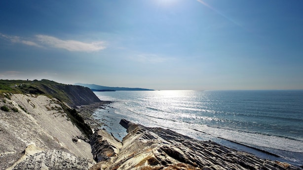 Un paisaje costero con una costa rocosa, cielo despejado y el océano hasta el horizonte.