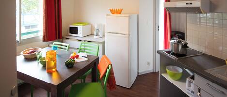 A compact kitchen with a dining table, chairs, a refrigerator, microwave, and a sink.