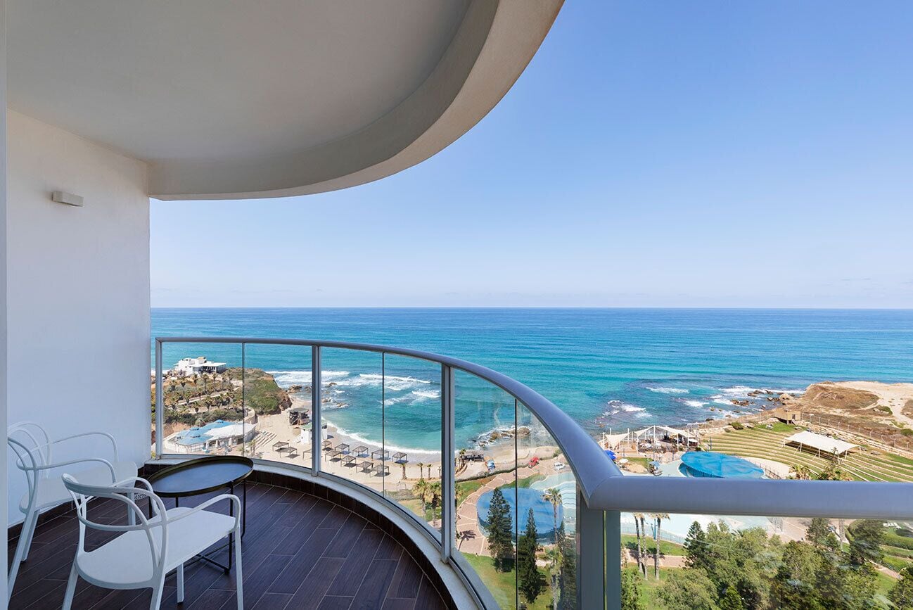 A balcony with a view of the ocean, a pool, and a beach area.