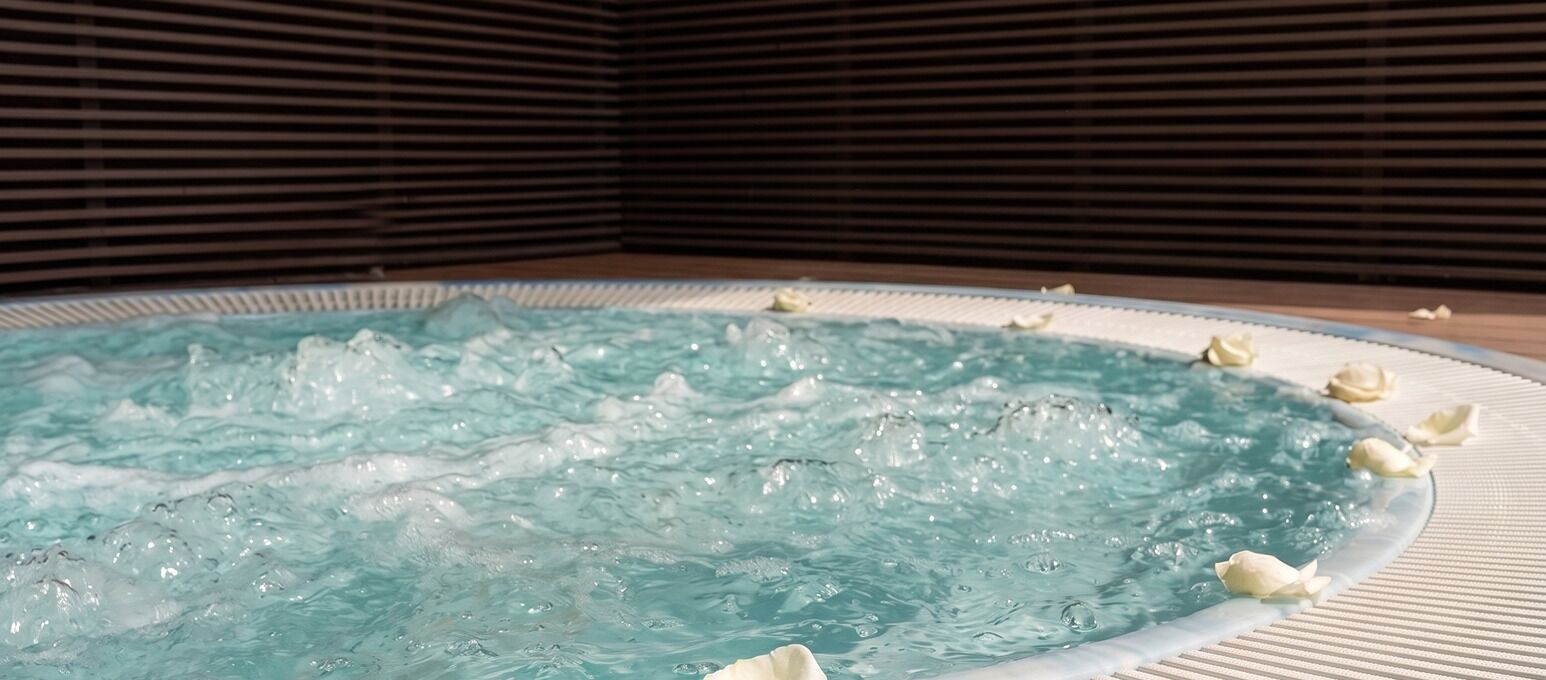 A hot tub with water jets, surrounded by a tiled floor and a wooden slatted wall.