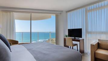 Een hotelkamer met een groot bed, een bureau met een televisie en uitzicht op de oceaan.