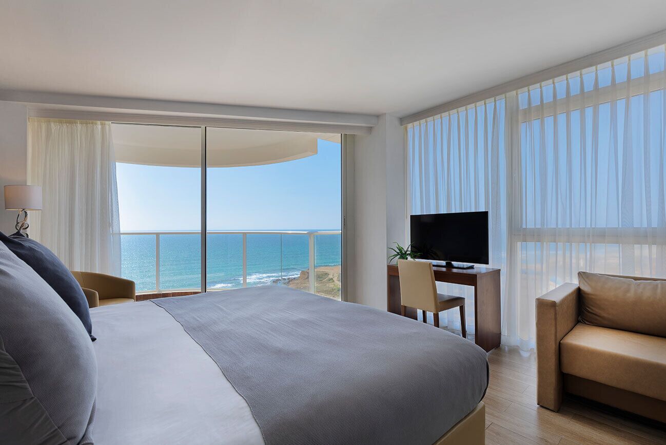 Ein Hotelzimmer mit einem großen Bett, einem Fernseher, einem Schreibtisch mit Stuhl und Blick aufs Meer.
