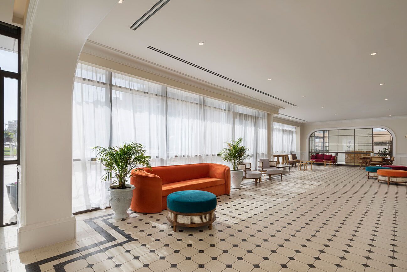 Um hall de hotel espaçoso, com uma grande janela, piso estampado e área de estar com sofá e banqueta.