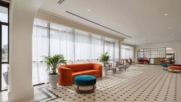 Um hall de hotel espaçoso, com uma grande janela, piso estampado e área de estar com sofá e banqueta.
