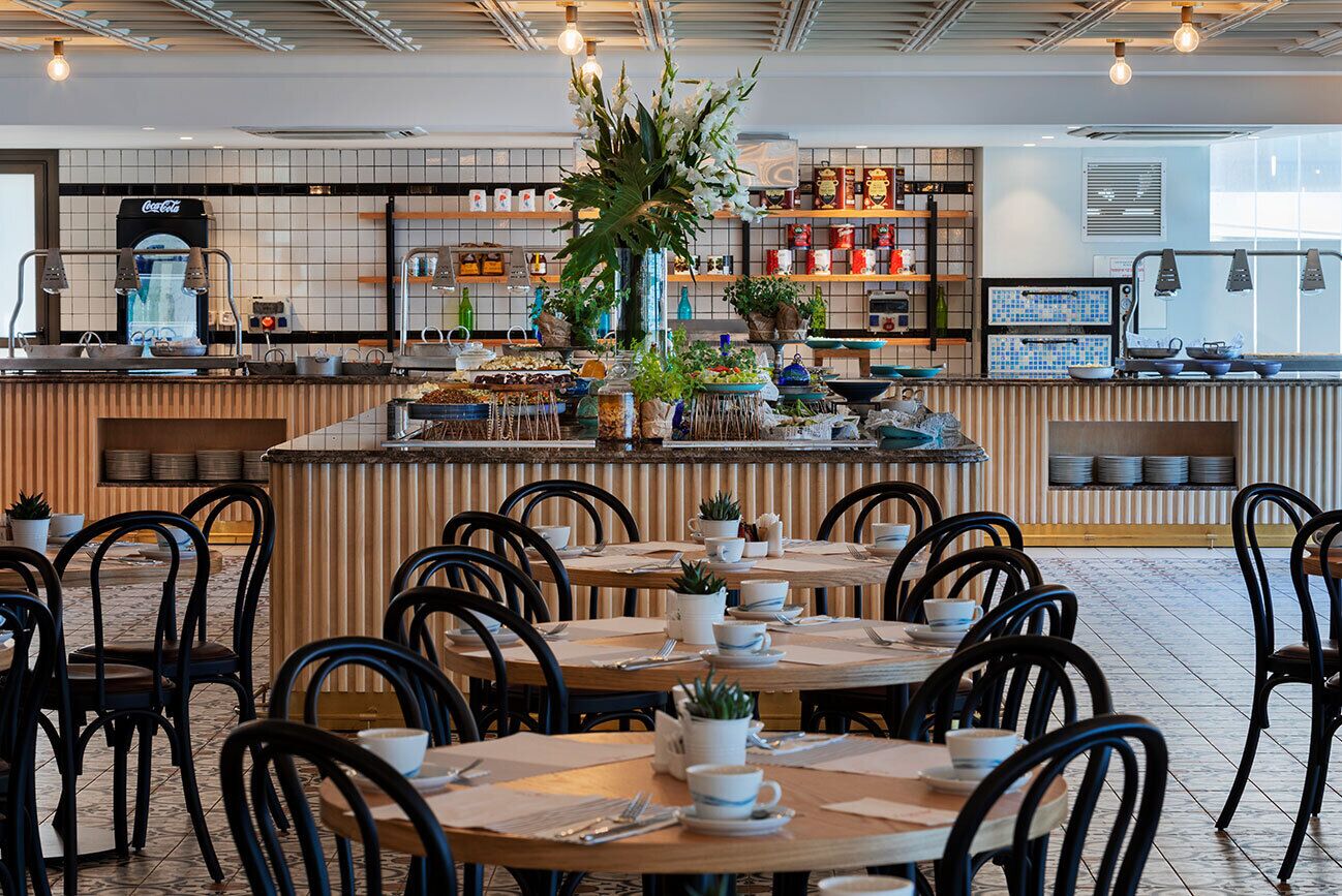 A restaurant with a central island, multiple tables, chairs, and a variety of plants and kitchen equipment.