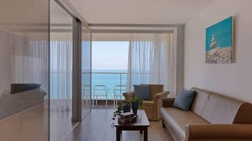 A modern living room with a sofa, chairs, a coffee table, and a view of the sea through large windows.