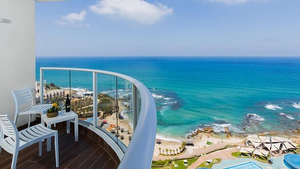 A balcony with a view of the ocean, a table with a bottle, and white chairs. - Resort Hadera Hotel By Jacob (Hadera)