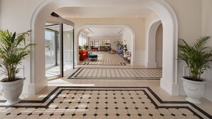 A hotel lobby with a geometric patterned floor, white columns, and potted plants. - Resort Hadera Hotel By Jacob (Hadera)