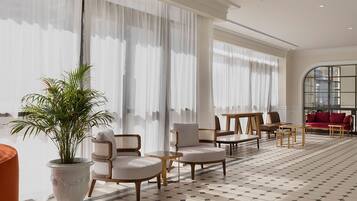 A hotel lobby with a checkered floor, large windows with sheer curtains, a potted plant, and a red sofa.