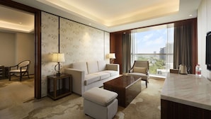 Una habitación de hotel moderna con sofá, sillones, una mesa de centro y vistas a la ciudad.