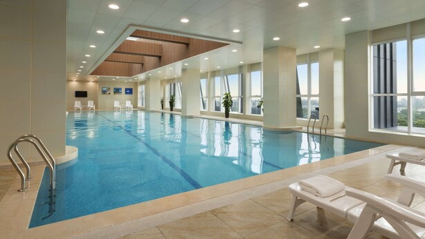 Una piscina interior con agua cristalina, un trampolín y sillones de descanso.
