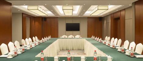 Un salón de conferencias con una larga mesa, sillas blancas y un televisor de pantalla plana.