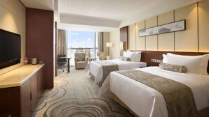 Habitación de hotel con dos camas, un escritorio con televisor, una silla y vista a la ciudad.