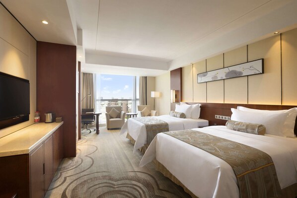 Habitación de hotel con dos camas, un escritorio con televisor, una silla y vista a la ciudad.