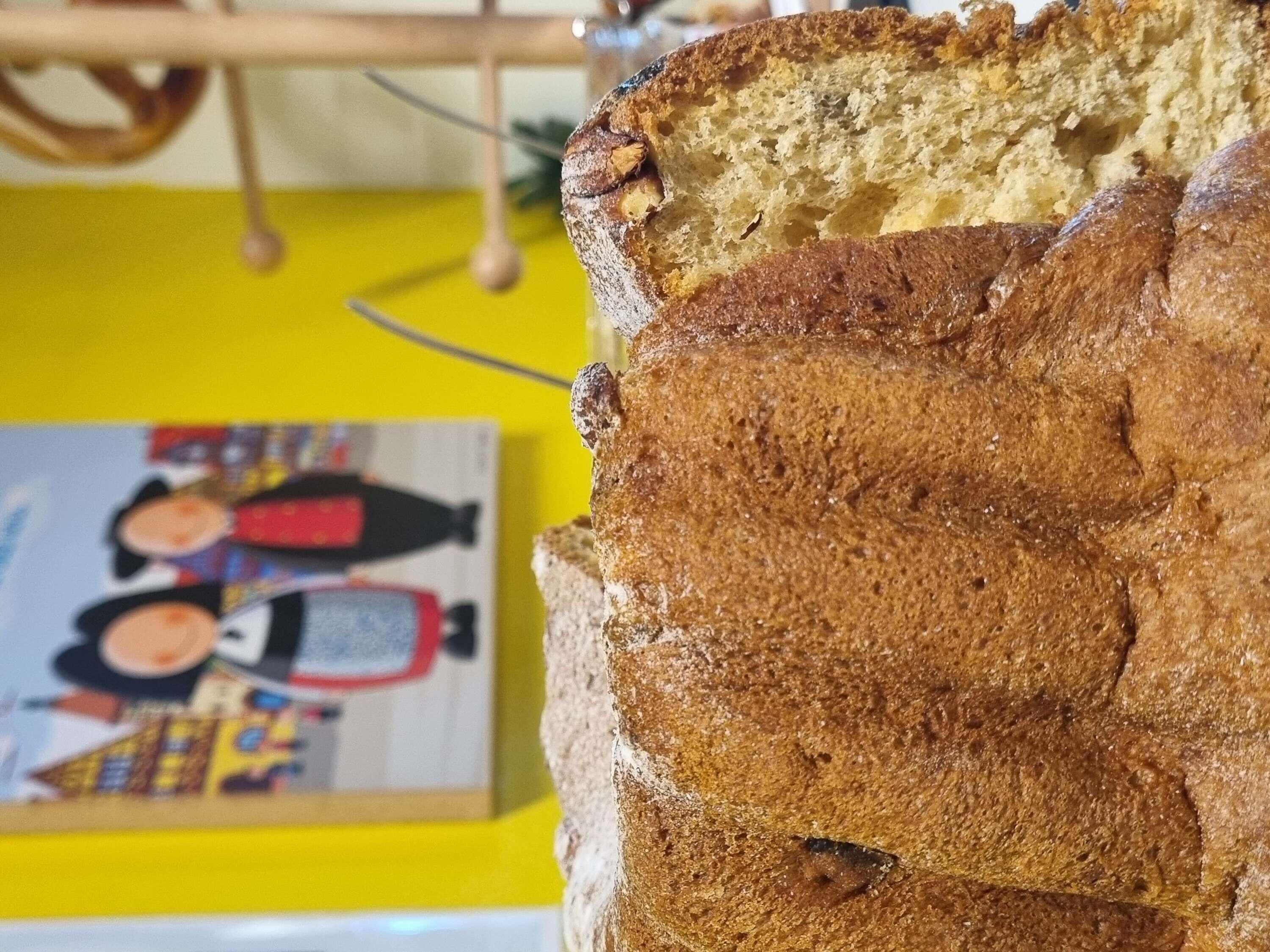 Una barra de pan con corteza crujiente, una rebanada cortada y un fondo amarillo con un objeto desenfocado.