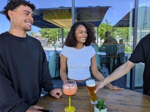 Un grupo de personas sentadas en una mesa al aire libre, con bebidas, una planta en maceta y una cerveza.