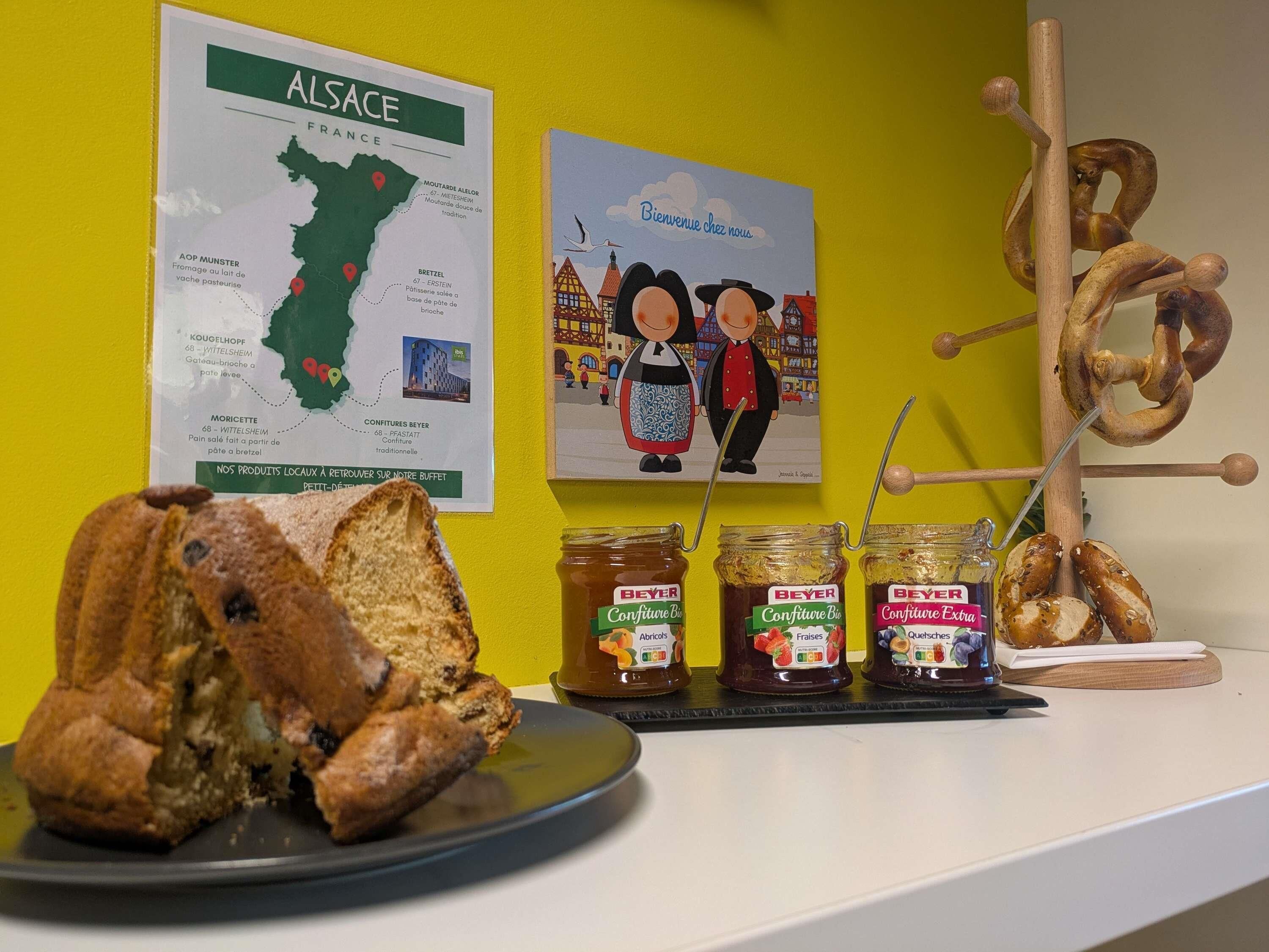 A table with a loaf of bread, jars of jam, pretzels, a map of Alsace, and a welcome sign.