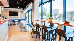 Un café moderno con barra, asientos y ventanas amplias que ofrecen vistas a la ciudad.