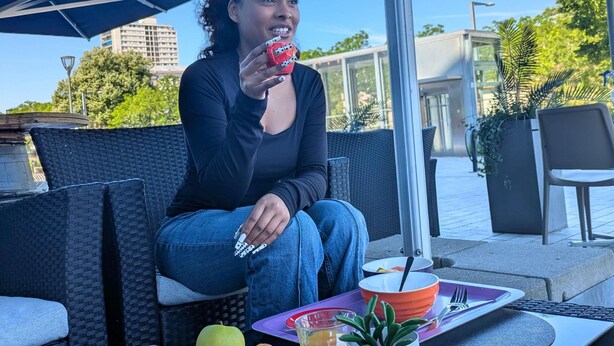 Una persona sentada en un café al aire libre, con una mesa, una bebida y un plato de comida.