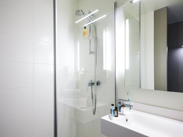 Un baño moderno con ducha de vidrio, lavabo blanco y un espejo grande.