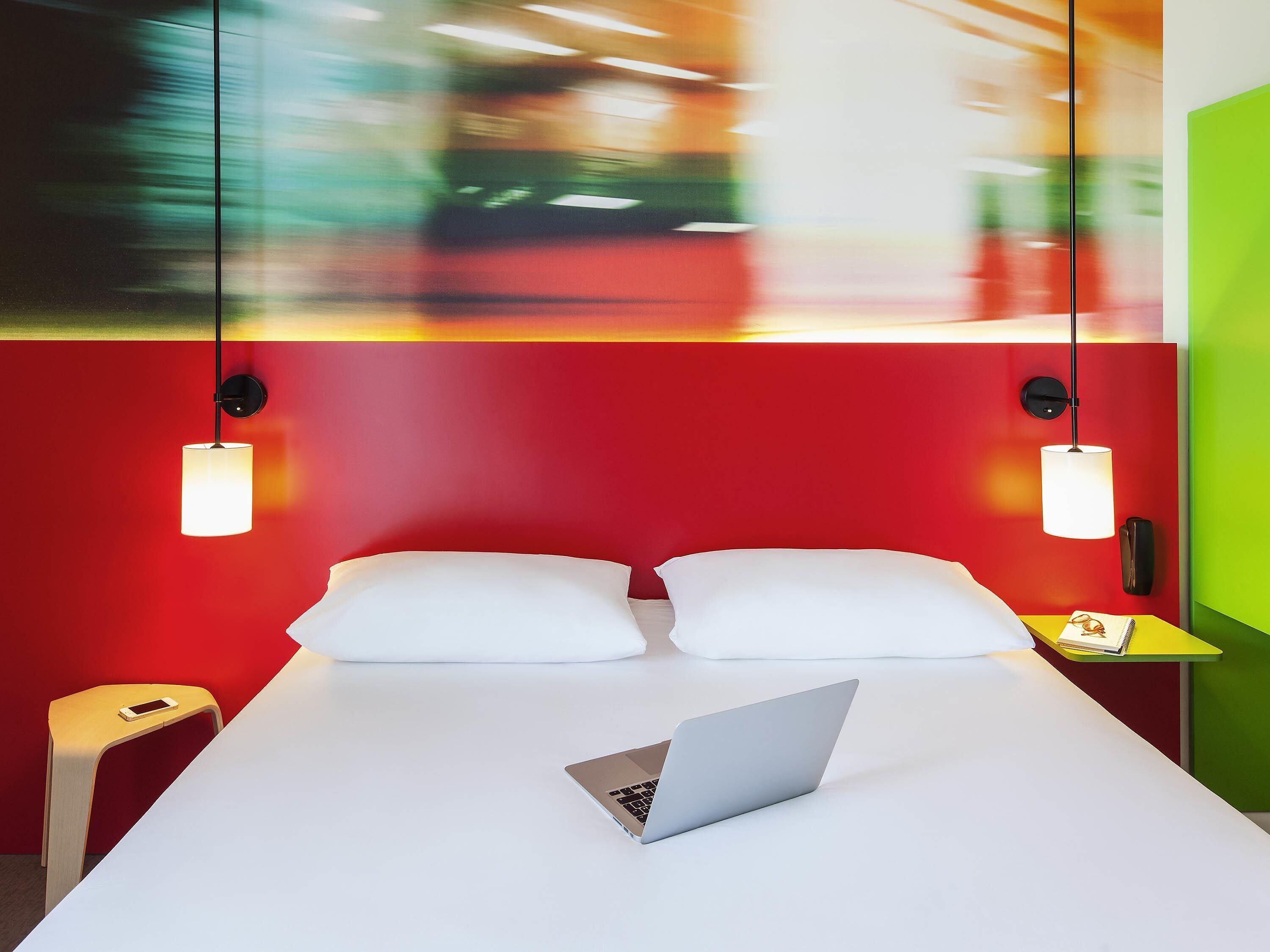 A modern hotel room with a bed, a laptop on the bed, and a nightstand with a phone.