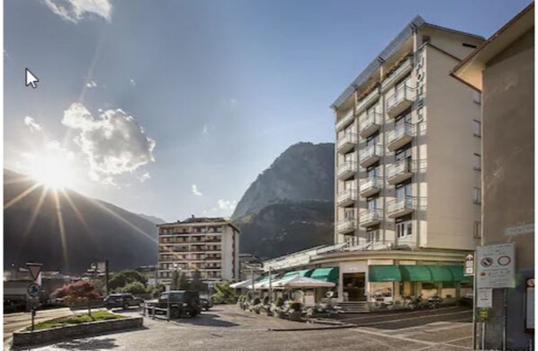 Un hotel de varios pisos, con mesas al aire libre y montañas al fondo.