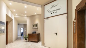 A hotel lobby with a large sign reading "Hotel Conradi," a wooden dresser, a potted plant, and a door with a keypad lock.