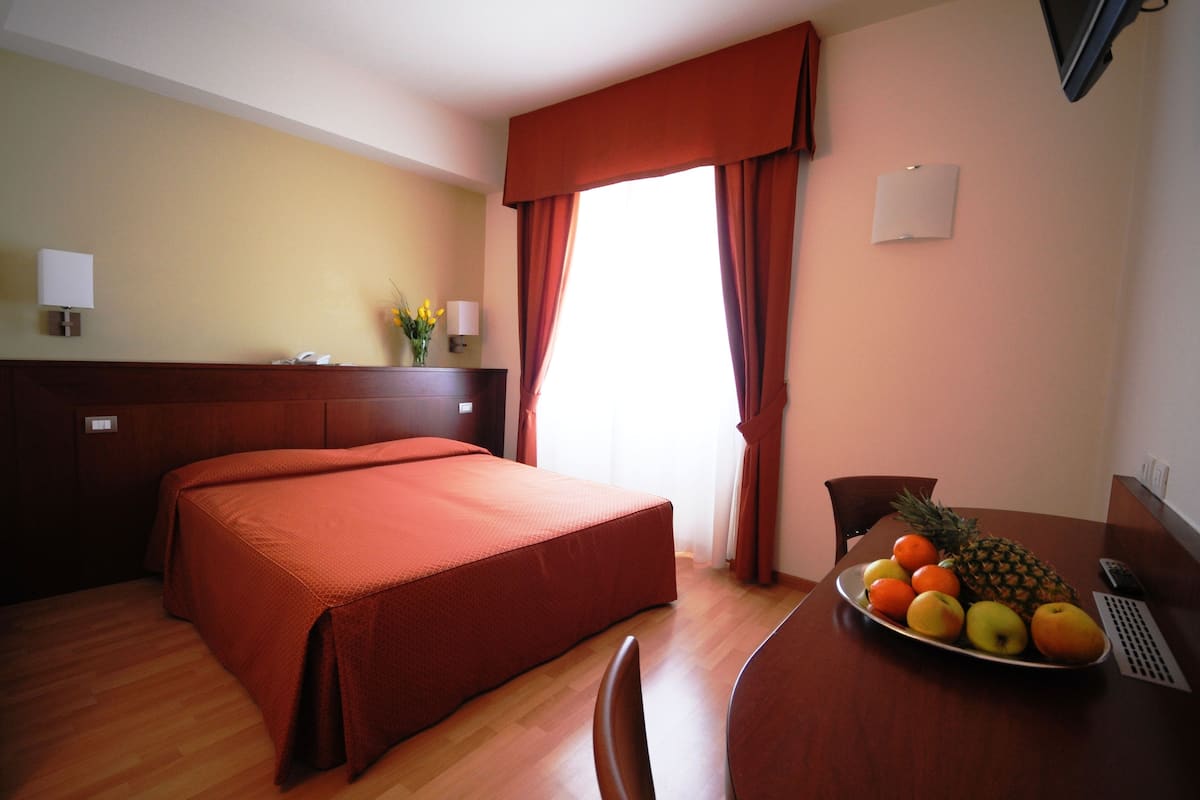 Une chambre d’hôtel avec un lit, une table à manger avec des fruits et une fenêtre avec des rideaux.