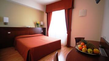 Une chambre d’hôtel avec un lit, une table à manger avec des fruits et une fenêtre avec des rideaux.