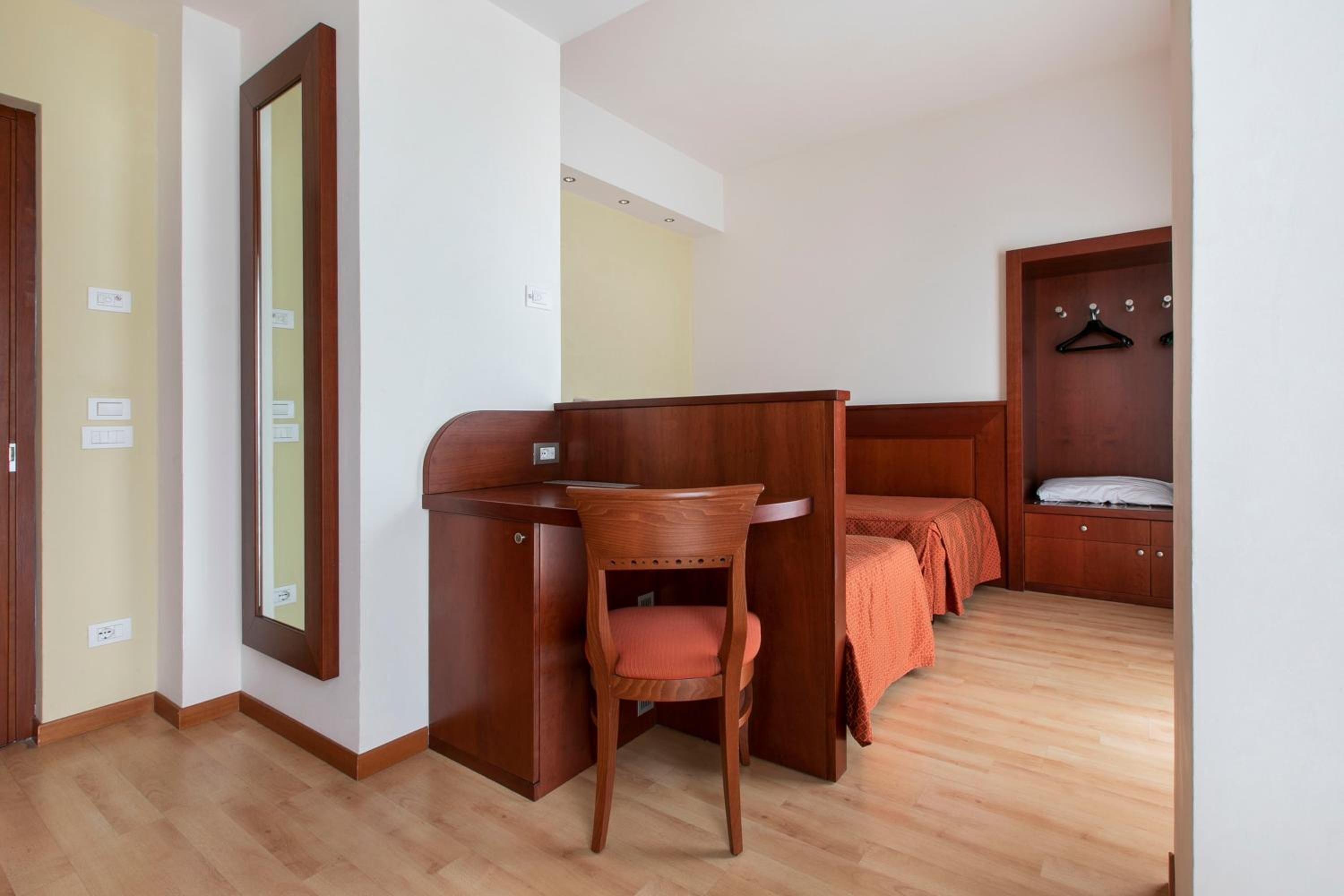 A bedroom with a wooden desk, a chair, a bed with a wooden headboard, and a wardrobe with a mirror.