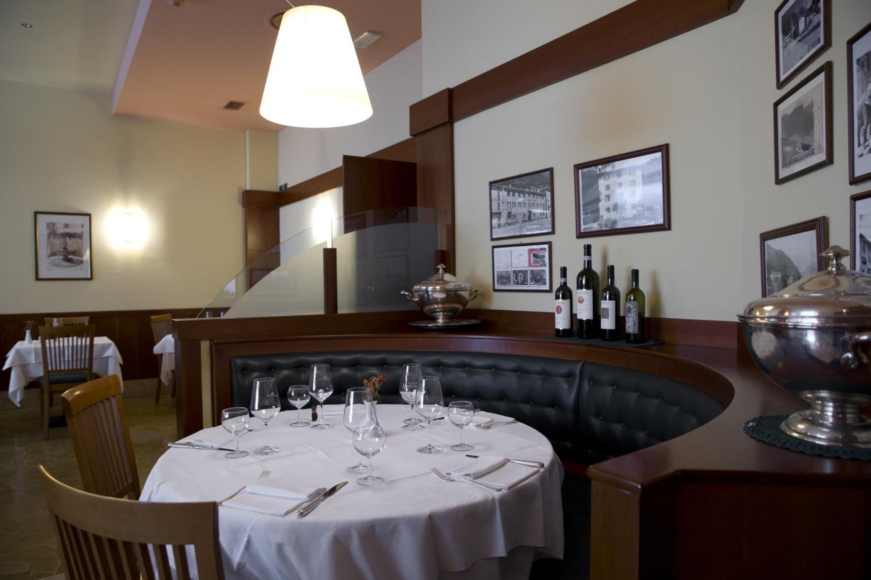 Un comedor con una mesa redonda dispuesta para cuatro personas, un banco de cuero negro y una hilera de botellas de vino en la pared.