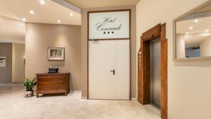 A hotel lobby with a sign reading "Hotel Conradi," a wooden cabinet, a potted plant, and an elevator.