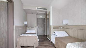 A hotel room with two beds, a wooden floor, a wardrobe, and a mirror.