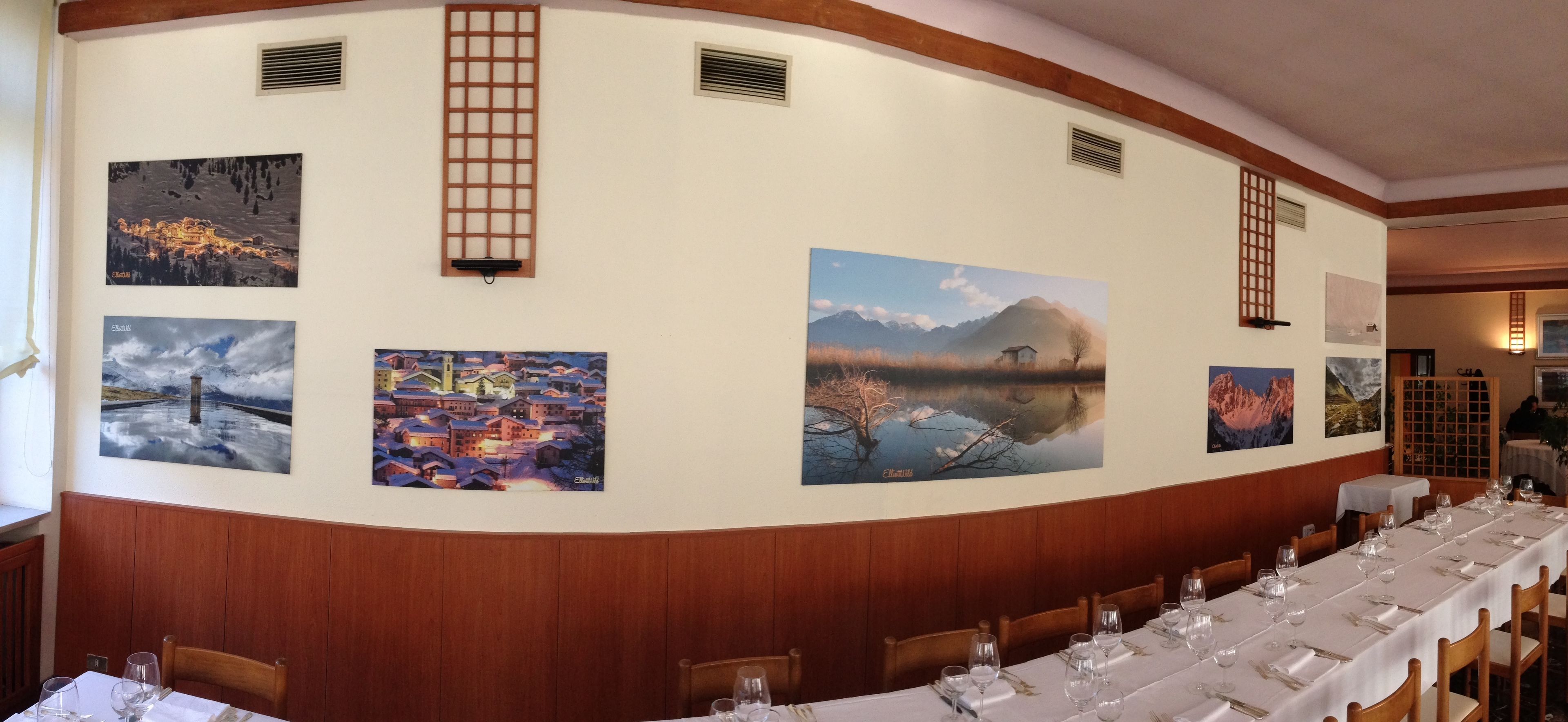 A restaurant with a long dining table set for a meal, surrounded by wooden paneling and artwork on the walls.