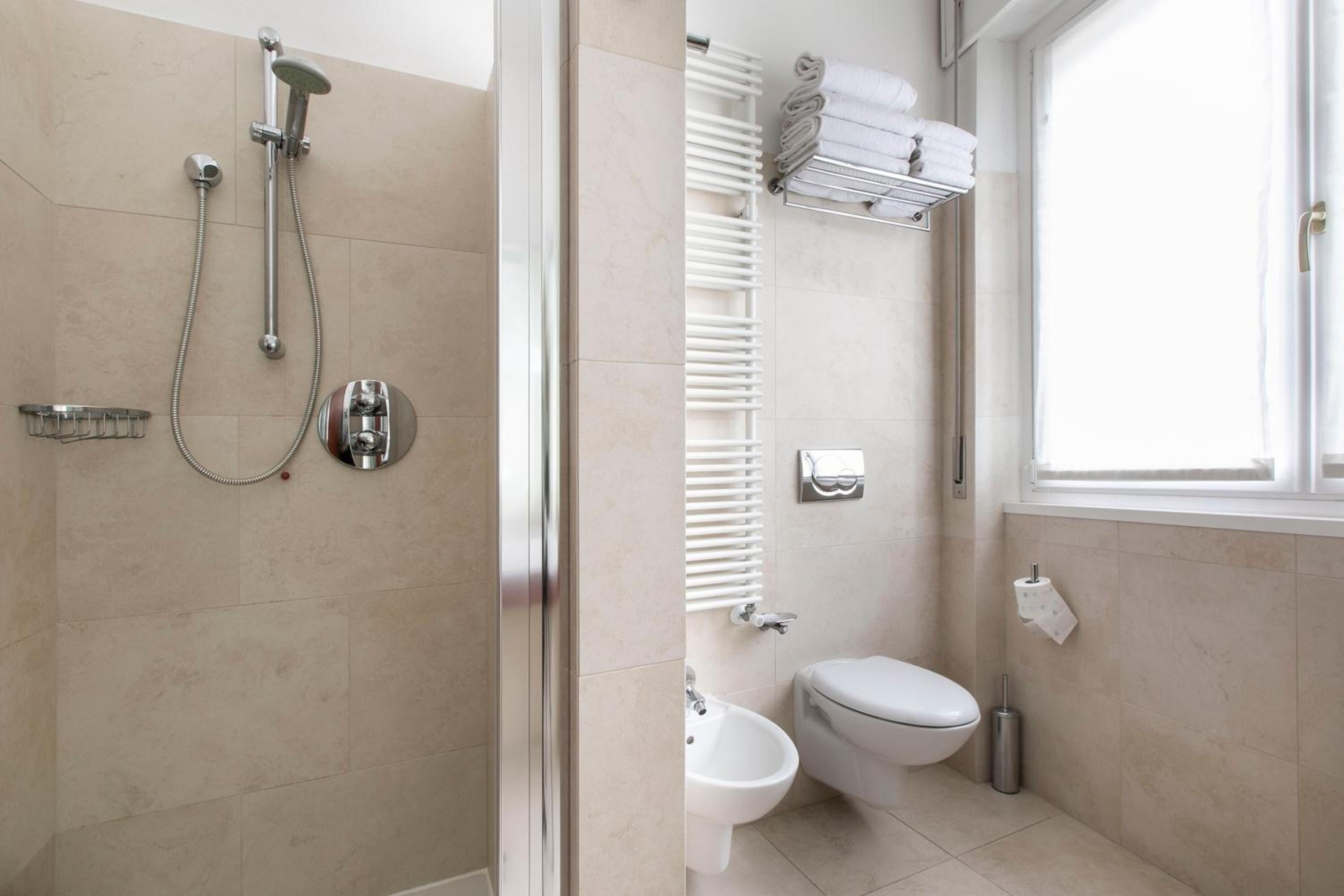 Uma casa de banho moderna com chuveiro, sanita, lavatório e suporte para toalhas.