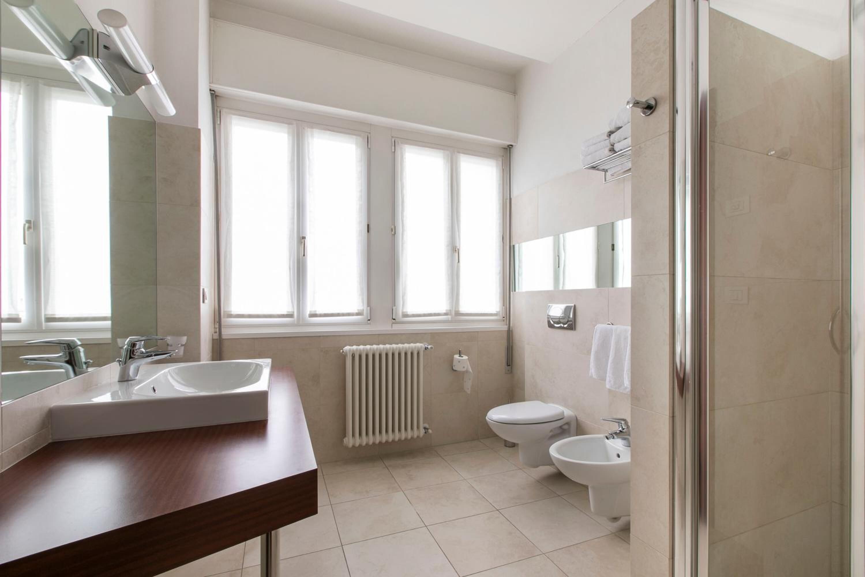 Ein modernes Badezimmer mit einem großen Spiegel, zwei Waschbecken, einer Toilette und einer Duschkabine.